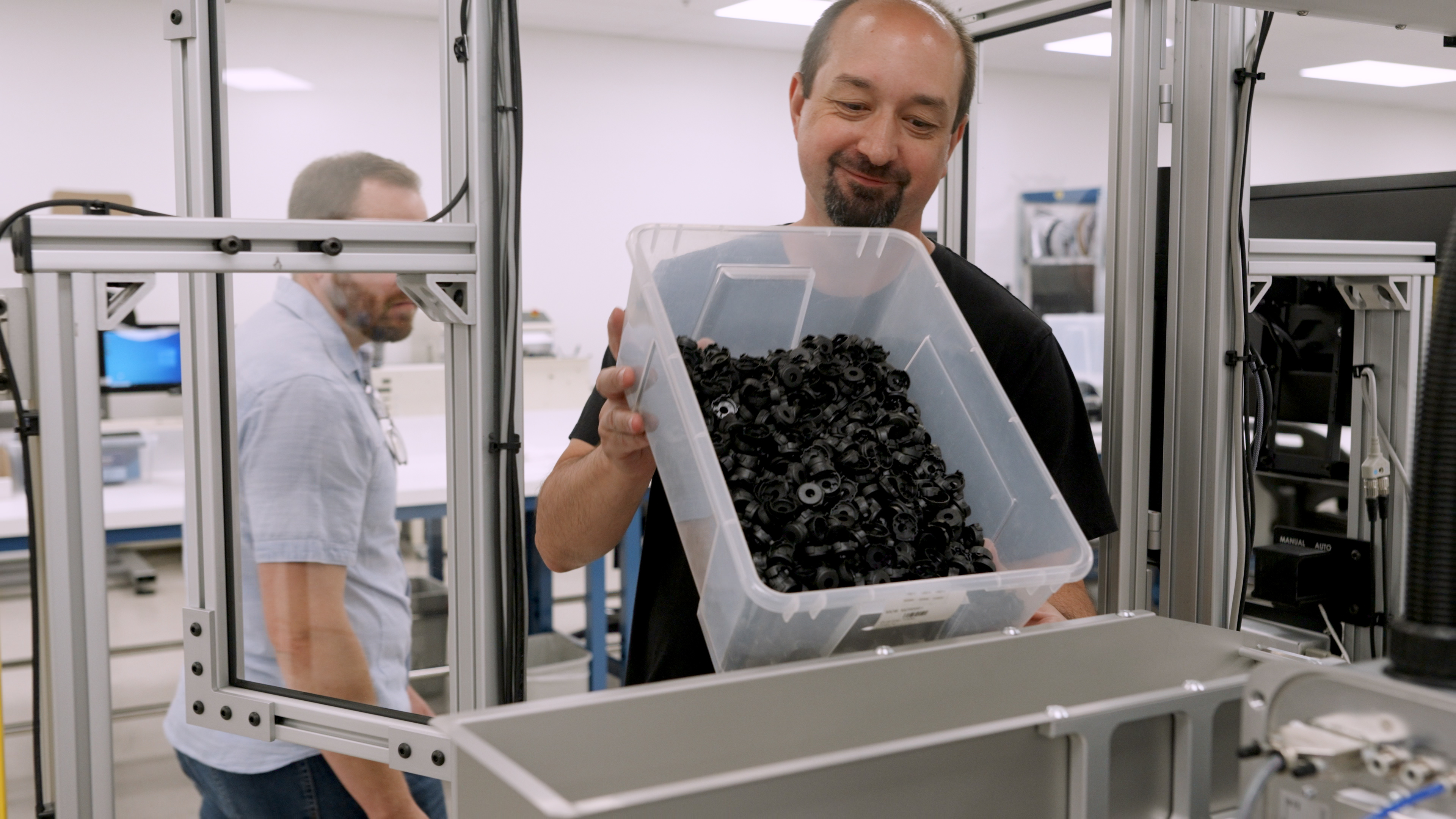 man pouring bin of plastic pieces into metal hopper