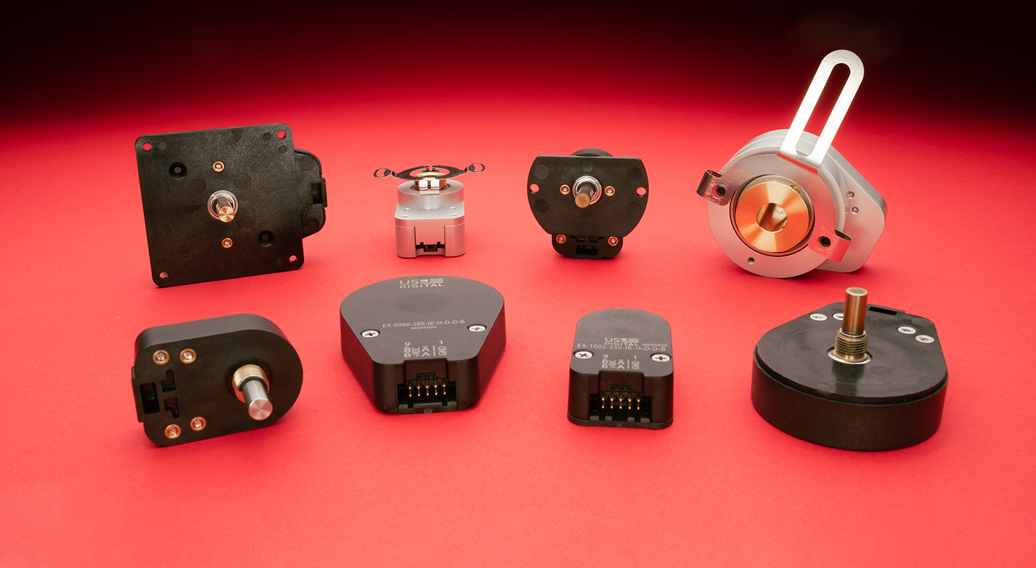 US Digital E5 and E6 series incremental optical encoders on a red paper backdrop